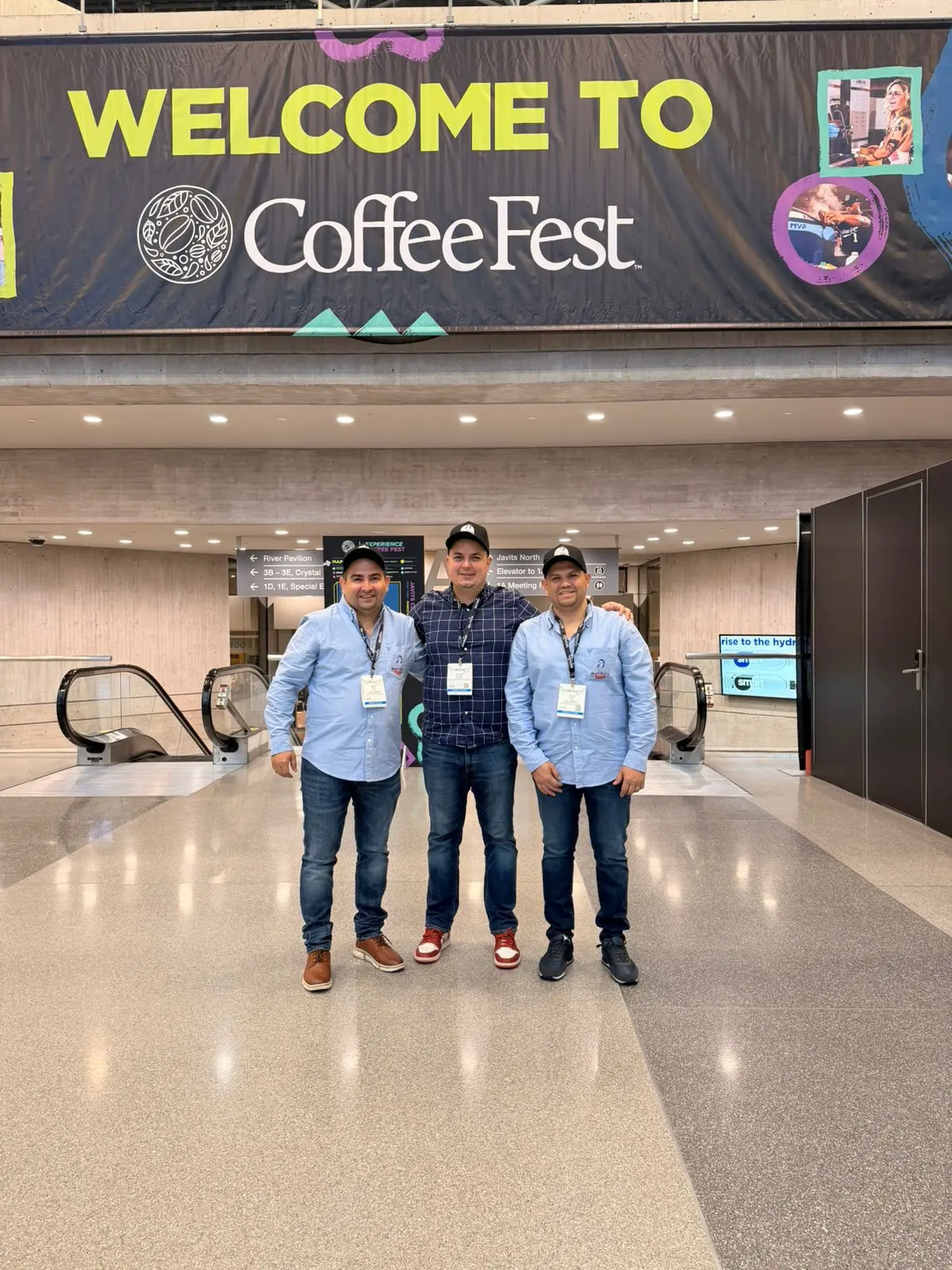Three producers standing under the Coffee Fest banner at the Javits Center